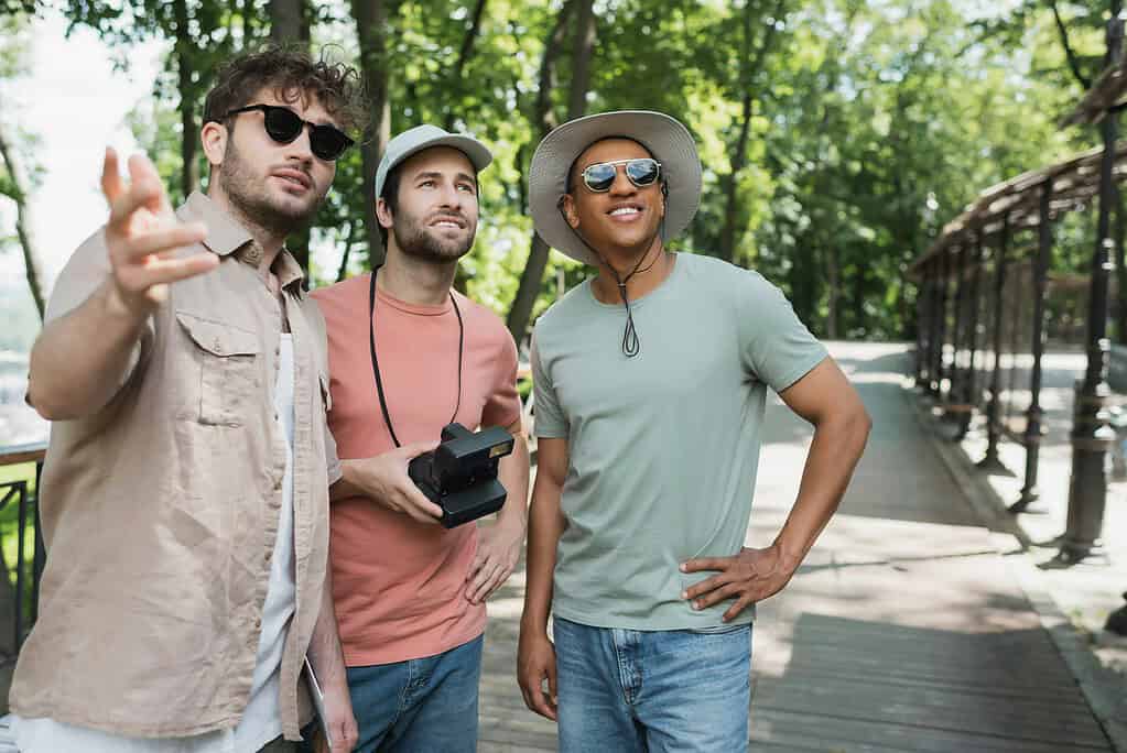 interracial travelers with vintage camera smiling and looking away near tour guide pointing with